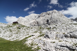 Zasavska koča na Prehodavcih (2071 m n. m.) se objevuje v dohledu, vlevo za ní v mraku pravděpodobně vrchol hory Triglav (2864 m n. m.)